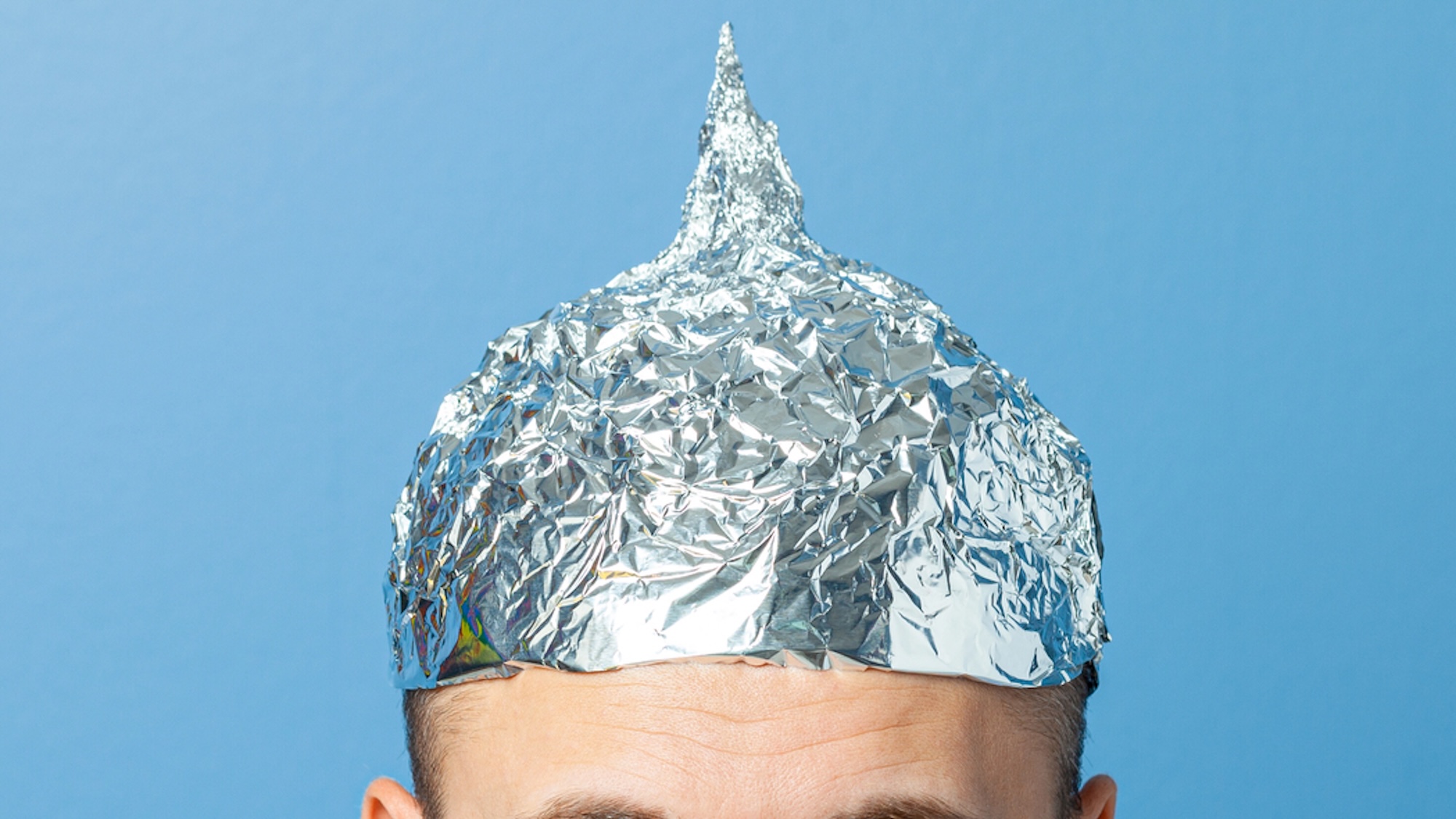 close up of tinfoil hat on man against blue background