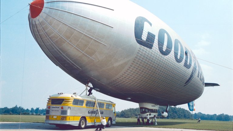 a blimp attached to a bus with a person holding a rope